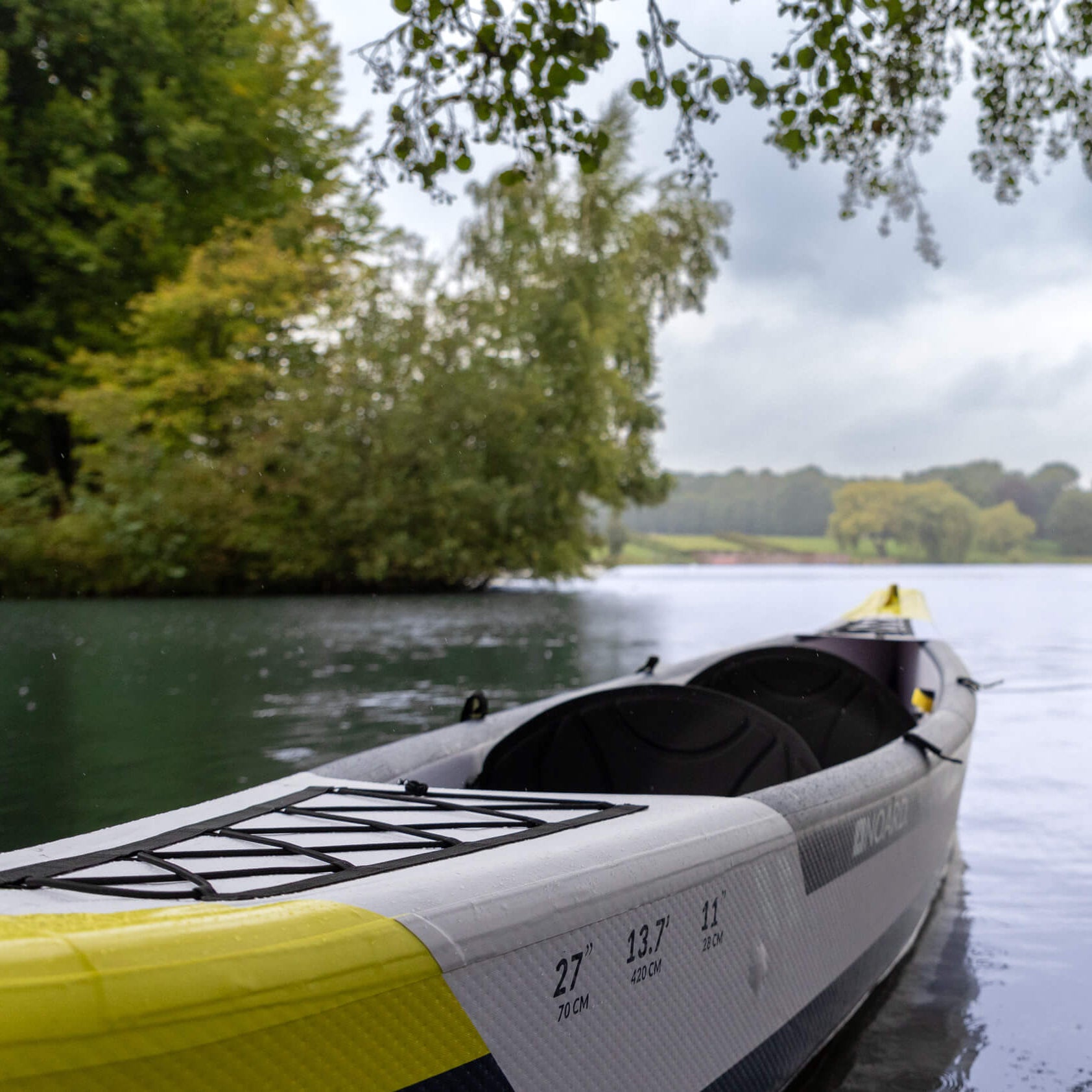 Noard Kajak Cruise schwimmt auf einem ruhigen Gewässer, umgeben von einer Baumlandschaft.