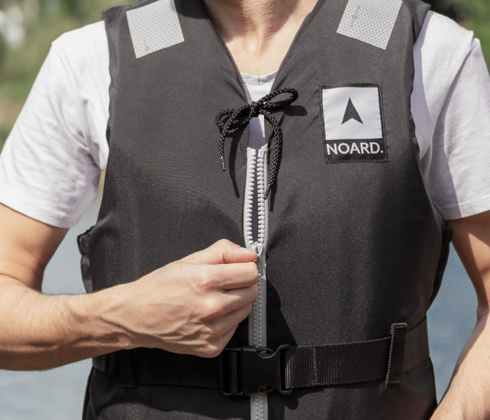 Ein Mann trägt eine NORD-Schwimmhilfe und zieht den Reißverschluss zu.